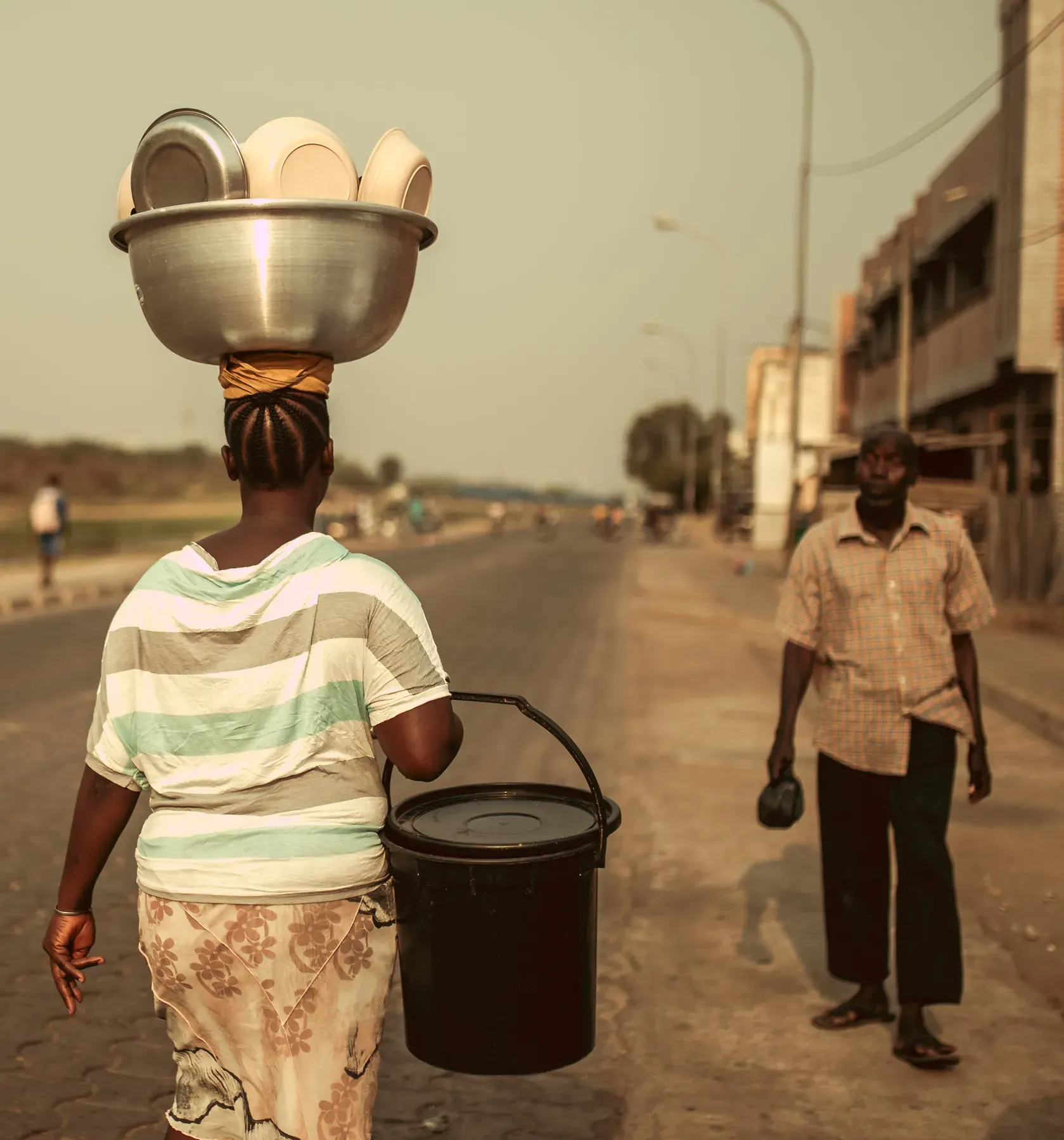 A woman carrying a basin on her head along a road.