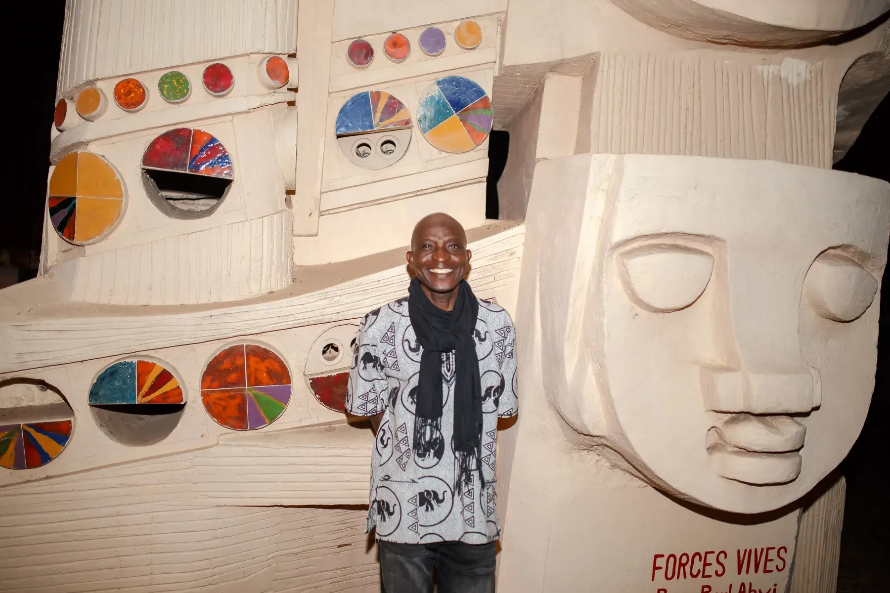 Richard Meseko in front of a sculpted mural with painted circles.