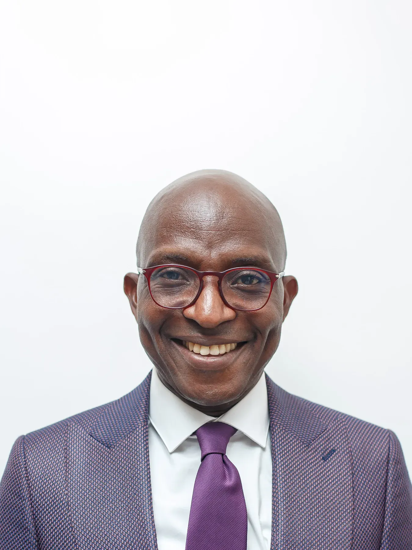 Head-and-shoulders portrait of Richard Meseko smiling, in glasses and a suit.